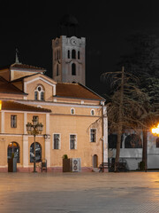 night shot of an orthodox church and a historic bell tower with a clock, featuring warm illumination on the stucco facade and a dark sky backdrop