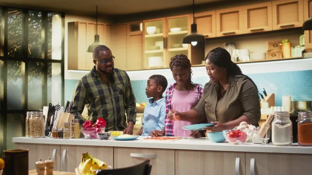Smiling parents and kids learning to make pizza from a homemade family recipe, mom and dad involving little helpers children to teach culinary hobby. Bonding and laughter during weekend. Camera A.