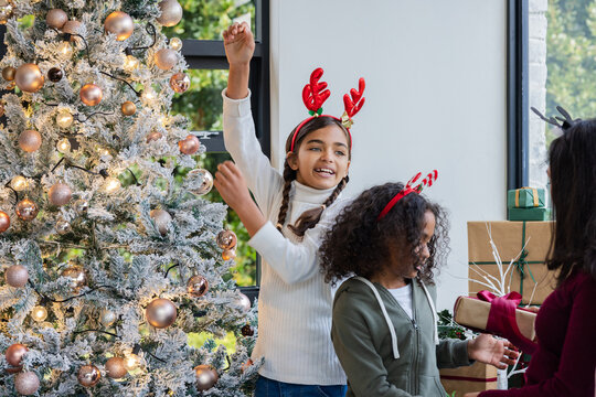Diverse family exchanging gifts in living room near Christmas tree with presents, antler headbands