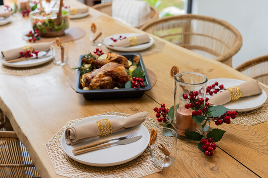 Black roasting tray is holding turkey with herbs on table with white plates and napkins