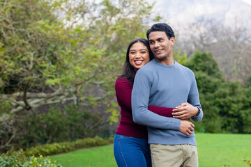 Diverse couple hugging on lawn at public park in burgundy and blue sweaters, copy space