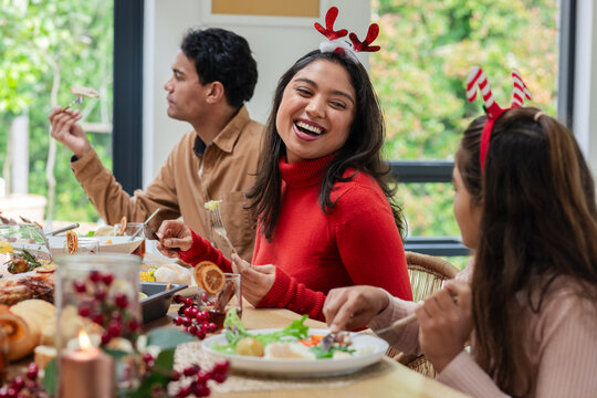 Family sharing holiday dishes in dining room around wooden table wearing reindeer headbands