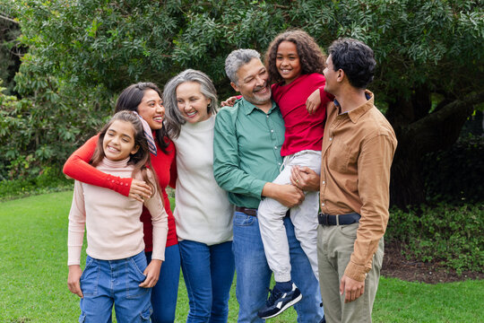 Diverse family linking arms and smiling on backyard lawn before leafy tree backdrop