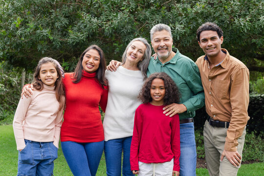 Senior couple with adult children and grandchildren standing together on lawn under leafy tree