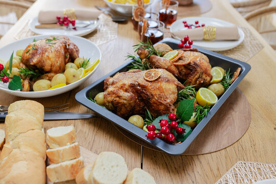 Dining table showcasing black roasting pan with roasted chickens, potatoes, citrus and rosemary