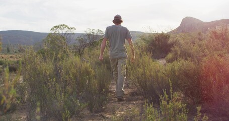 Lone hiker wearing gray shirt and khaki pants walking away on dirt trail in canyon valley