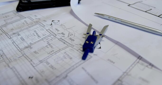 Featuring drafting compass resting on blueprints at studio desk, with silver pen and tablet