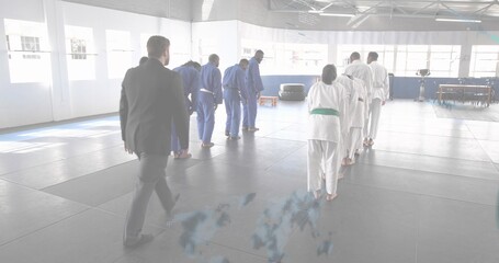 Walking instructor in dark suit approaching bowing martial artists on dojo mats, with gis and belts