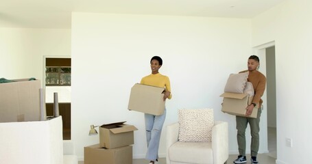 Couple wearing casual clothes carrying moving boxes in living room with wrapped furniture