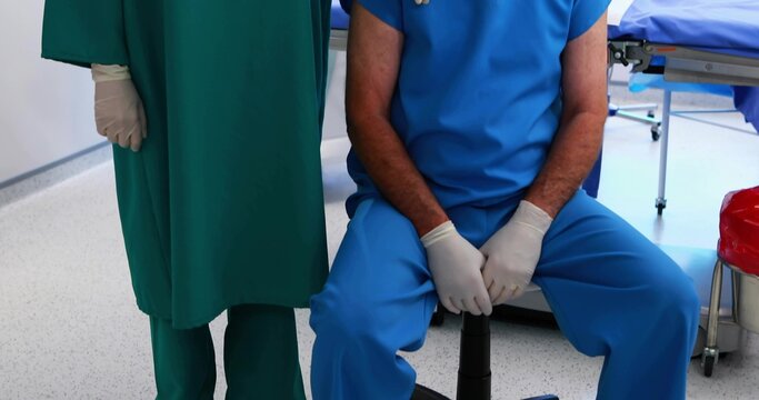 Nurse and surgeon preparing tools in operating room, with blue table, gloves and red waste bin - Powered by Adobe