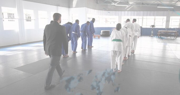 Walking instructor in dark suit approaching bowing martial artists on dojo mats, with gis and belts