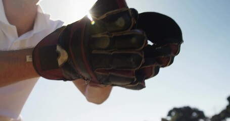Fototapeta premium Holding padded glove toward camera on sports field, showing white polo sleeve and sun halo