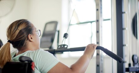 Gripping woman in wheelchair wearing mint tee and glasses using lat pulldown at gym, copy space