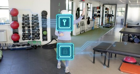 Standing adult woman gesturing toward AR holograms at gym, wearing white cap and gray leggings