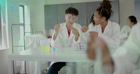 Mixing students handling test tubes with pipette at school lab bench, white lab coats and goggles