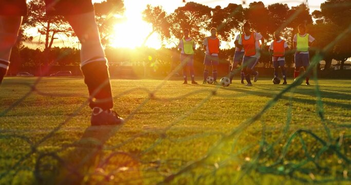 Framing cleated foot through goal net at soccer pitch, with multiple balls and bibs, copy space