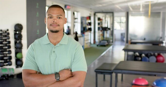 Posing man in green polo crossing arms facing camera at gym, with weights, smartwatch, copy space