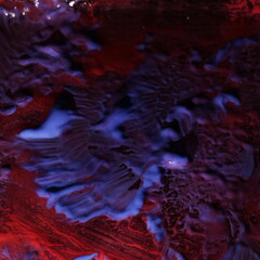 Una toma de cerca de un fondo abstracto de varias manchas de pintura con agua y aceite de color azul y rojo colocada en un pote de vidrio con algo de desenfoque