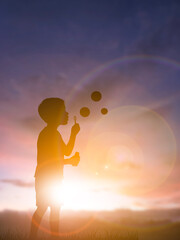 Silhouette of a boy blowing soap bubbles at sunset with warm sunlight and bokeh in the background