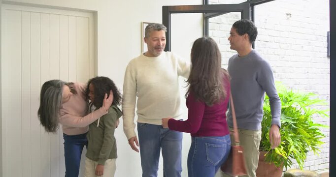 Glass door swinging inward as diverse family handing gift box and hugging visiting family entryway