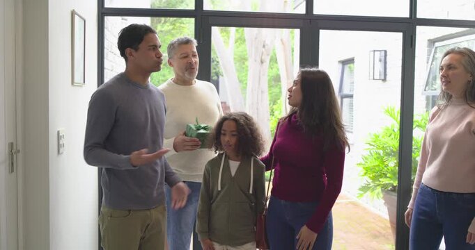 Family welcoming returning son arrival at foyer, offering green gift box and pointing ceiling light