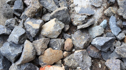 Pile of rocks sits on concrete surface, showing various shapes and textures under bright daylight, creating a rugged and natural scene.