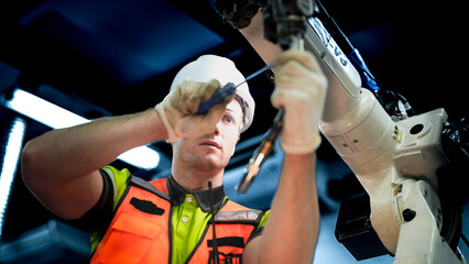 An engineer programs or repairs a high-tech industrial robot. This smart factory uses AI-driven automation for advanced manufacturing or microchip production.