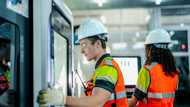 A male and female engineer in hard hats and safety vests operate a high tech machine. They are collaborating in a futuristic smart factory. - Powered by Adobe