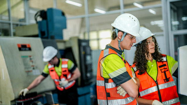 A happy, diverse team of engineers in hard hats and safety vests. They are in a modern smart factory, collaborating near a large industrial machine.