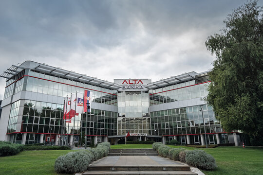 BELGRADE, SERBIA - AUGUST 31, 2025: Front view of the glass-fronted Alta Banka headquarters in Belgrade, with flags and landscaped approach. Alta banka is a Serbian commercial and retail bank.
