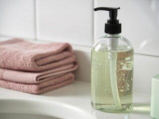 Soap dispenser and towels on a bathroom sink with white tiled background