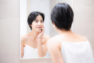 洗面台で鏡を見ながらスキンケアする女性