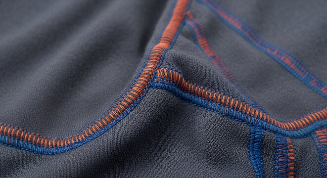 Close-up of a dark gray fabric with vibrant orange and blue stitching, creating a dynamic and textured pattern.