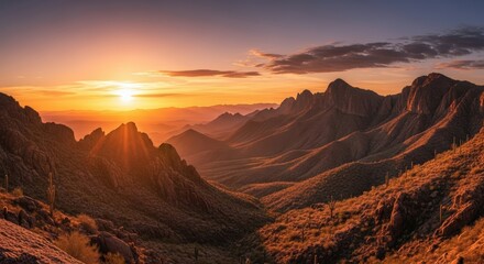 Fototapeta premium Dramatic Sunset Over Rugged Desert Mountains With Silhouetted Cacti And Distant Valley