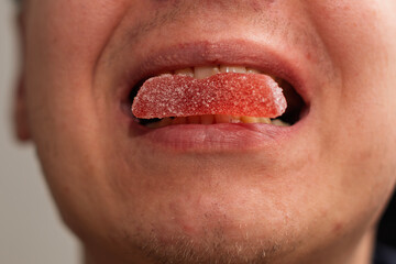A person holds a large, brightly colored, sugar-coated gummy sweet between their lips, showing the...
