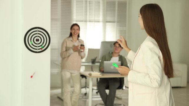 Woman playing darts and her colleagues in office, selective focus