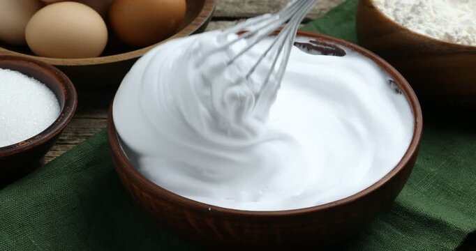 Whisking egg whites at wooden table, closeup