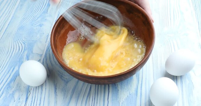 Woman whisking eggs in bowl at light blue wooden table, closeup
