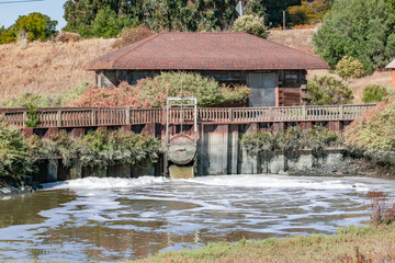 Water treatment facility with red roof, valve platform, and foamy water near vegetation