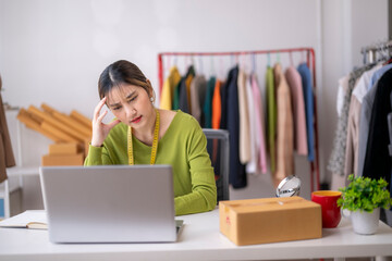 Asian fashion designer having problems with online business using laptop in her studio