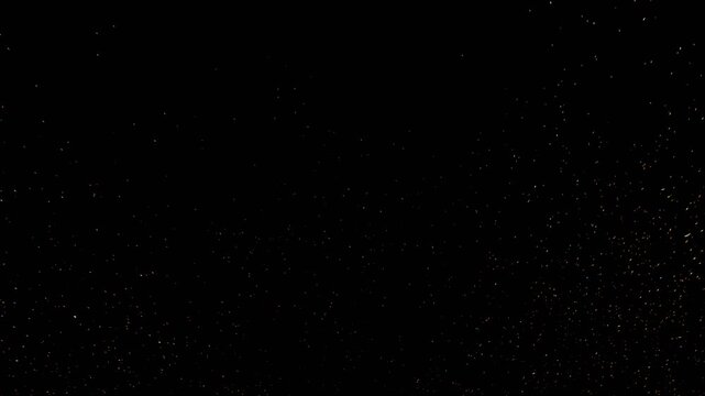 A very dark, almost black background with subtle, fine white speckles scattered across the surface, resembling dust or distant stars.