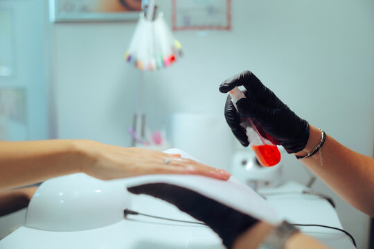 Nail Expert Using a Disinfectant Spray in the Hands of her Client. Manicurist following safety protocols using disinfecting solution before work