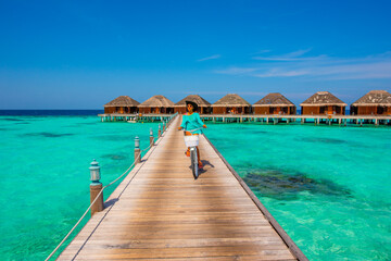 Woman riding bicycle. Tropical island beach landscape exotic shore coast. Tranquil closeup calm sea water waves with palm trees. Holiday amazing nature. Relax paradise, Maldives.