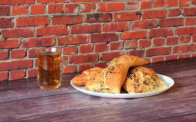 Large plate with several meat pies samsa decorated with caraway seeds and a cup of hot tea on a wooden table.
