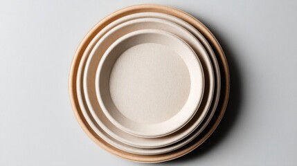 Stack of three circular, biodegradable, light tan colored plates on a light gray surface, from above
