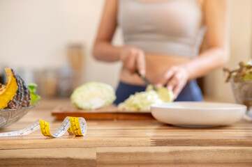 Close up of measuring tape on kitchen cooking counter and blurred sportswear woman cutting vegetable