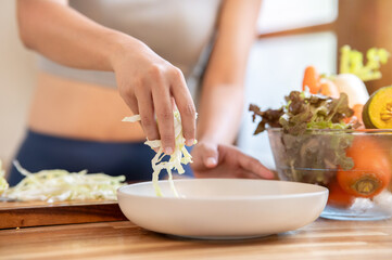 Close up of sportswear woman's hand holding shred cabbage over a plate at kitchen cooking counter.