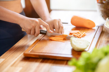 Close up sportswear woman holding knife cutting carrot on chopping board at kitchen cooking counter.