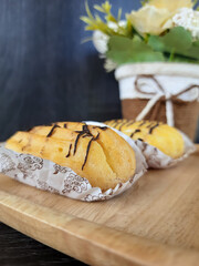 eclair choux pastry with chocolate topping on a wooden stand with baking paper as a base on a wooden background