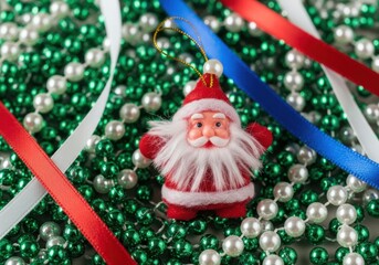 Closeup of a santa claus ornament nestled amongst green and white pearl beads and red and blue ribbons, a festive holiday decoration